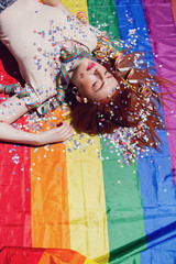 Chica joven y pelirroja después de una fiesta tumbada sobre una bandera arco iris 