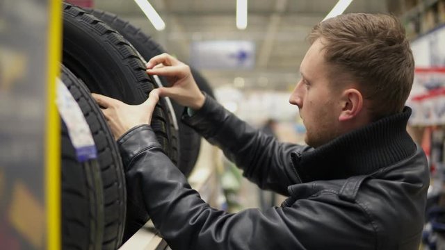 Young man looking over automobile tyres in the automotive department of the hypermarket and trying to choose while pressing on them