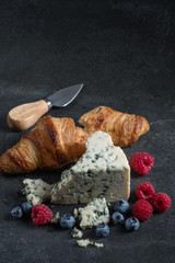 Tasting cheese with croissant bread and fresh berries on stone dark black background.