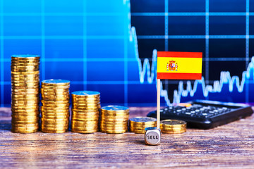 Downtrend of stacks of gold coins, flag of Spain, dice cube and calculator