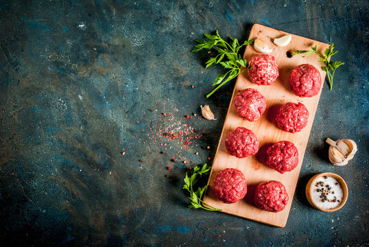 Raw meatballs with olive oil and spices on dark concrete table, top view copy space