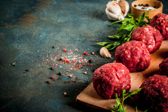 Raw meatballs with olive oil and spices on dark concrete table, copy space