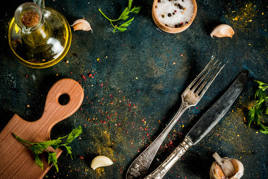 Cooking food concept, spices, herb and oil for preparing dinner, with cutting board, table knife and fork, copy space top view frame