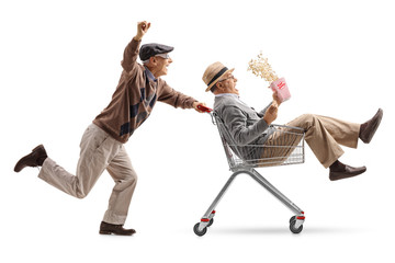 Senior with 3D glasses pushing a shopping cart with another senior with popcorn riding inside