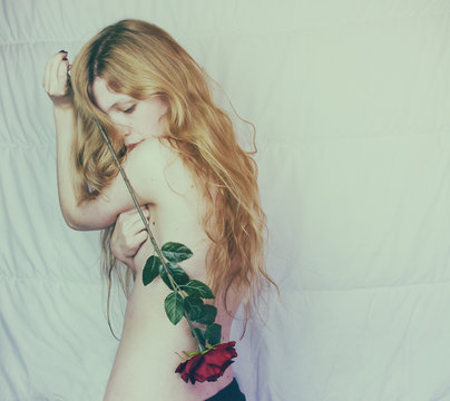 Mujer joven y rubia vista de espaldas sujetando una rosa roja 