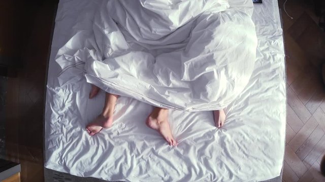 couple in bed making love. male and female legs top view, white linens. sex, 4k