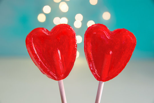 Two Red Heart Shape Candy Lollipops on Sticks Turquoise Background with Sparkling Bokeh Lights. Valentine Romantic Love Greeting Card Banner Poster with Copy Space
