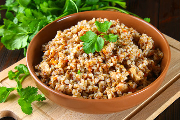 Boiled buckwheat in a bowl with pieces of chicken meat and cilantro on a brown wooden table.