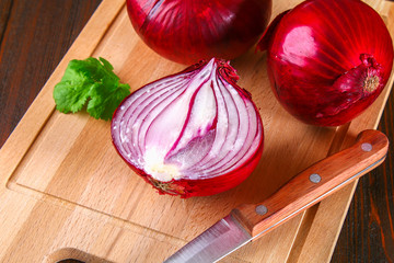 Fresh red onions and chopped slices on a wooden table.