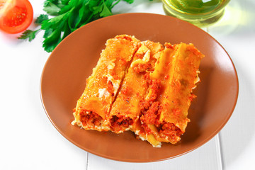 Traditional Italian pasta cannelloni. Baked tubes stuffed with minced meat with parmesan cheese and bechamel sauce on a white wooden table.
