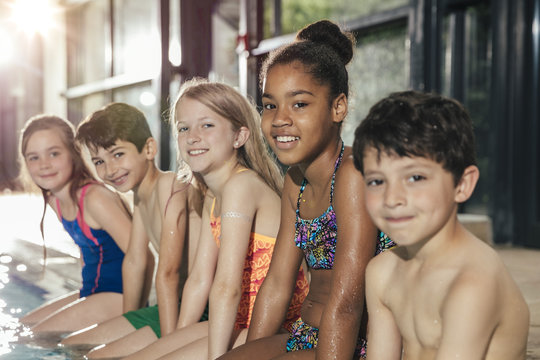 Portrait of smiling children sitting on poolside in indoor swimming pool