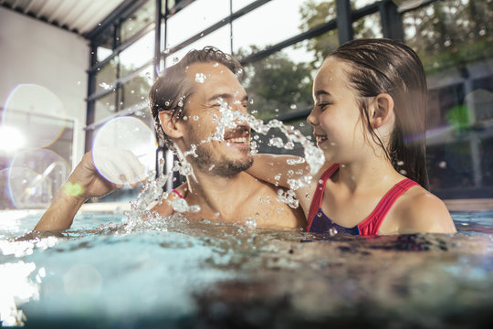 Happy father with daughter splashing in indoor swimming pool
