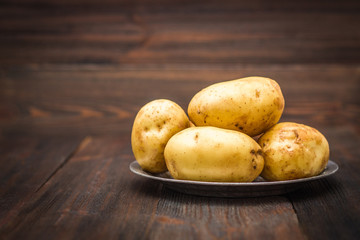 Raw potatoes on a brown wooden background.