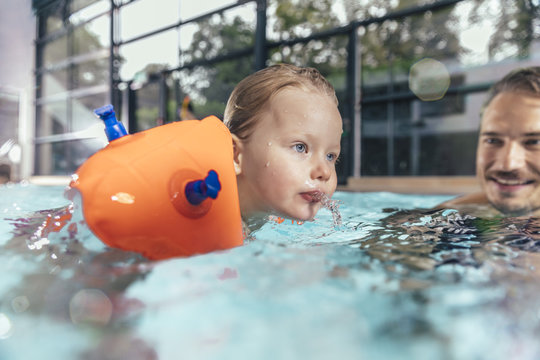Father with daughter wearing water wings in indoor swimming pool