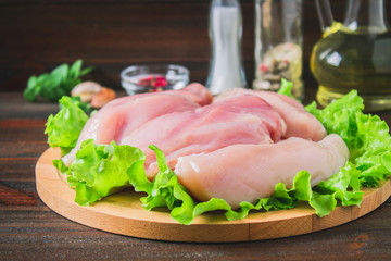 Raw chicken fillet and green salad on a round cutting board on a wooden table background. Meat ingredients for cooking.