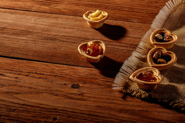Homemade tarts with dried fruits, nuts and jam on wood background.