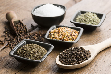 peppercorn in spoon with variety of other spices on wooden table.