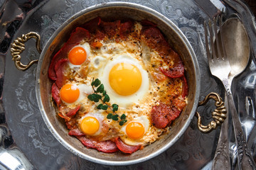 Closeup of Turkish pastirmali and fried egg in a copper pan on wooden table
