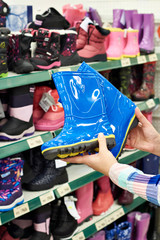 Fototapeta na wymiar Childrens rubber boots in hands of buyer at store