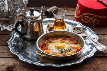 Fried egg with cured meat, traditional turkish breakfast, served in metal dishware, rustic