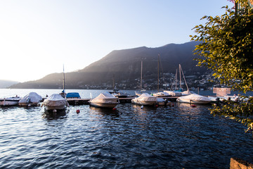 Fototapeta na wymiar Small port of a town on Lake Como with storage of fishing boats and berth for ferries for public transport on the lake. Lights at sunset from the port of the village of Torno on Como Lake