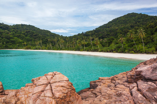 Wild beach with white sand and turquoise sea surrounded with granitic boulders and tropical greenery, Redang island, Malaysia