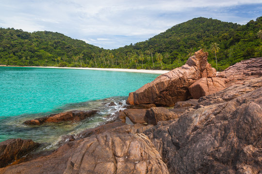 Wild beach with white sand and turquoise sea surrounded with granitic boulders and tropical greenery, Redang island, Malaysia
