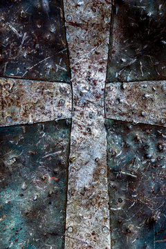 Detailed close-up photo of a christian cross symbol on a rusty battered medieval armor