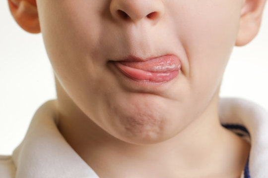 Studio shot of little boy's face, sticking out tongue