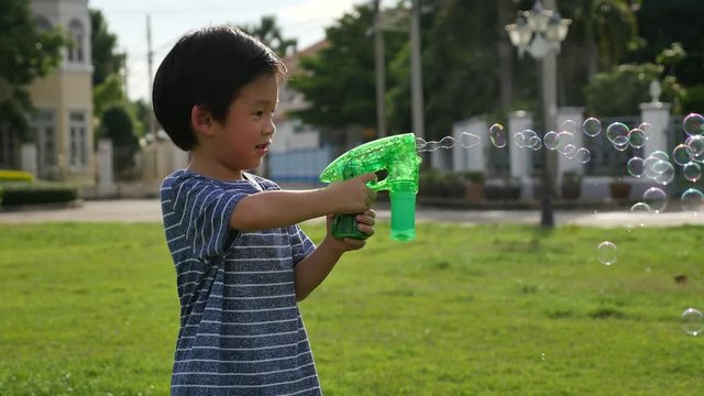 Cute Asian child Shooting Bubbles from Bubble Gun in the park