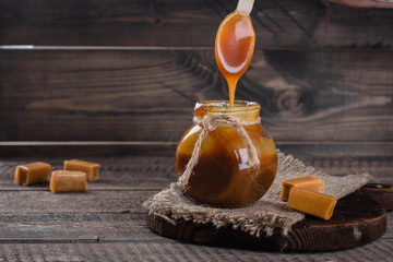 Homemade salted caramel sauce in jar on rustic wooden table background. Copy space.