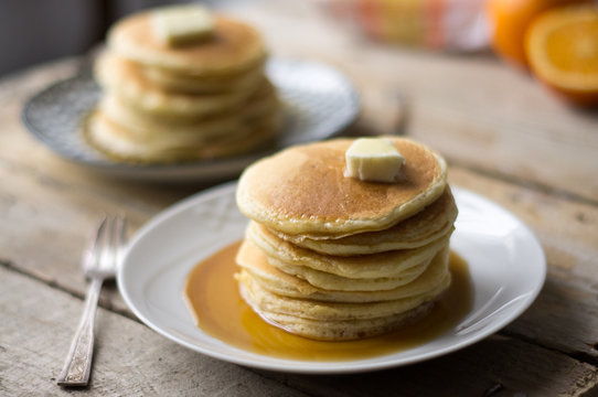 Two plates of homemade pancakes with. aple syrup and butter served on the wooden table