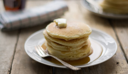 Homemade little pancakes with topping (maple strip and butter) on the plate on the wooden table