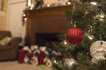 close up of Christmas tree decorations with a beautiful fireplace and stockings in the background
