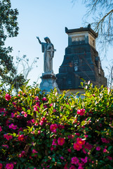 The sculpture of a woman with the cross, the stone crypt and bushes of flowers on the Oakland Cemetery in sunny autumn day, Atlanta, USA
