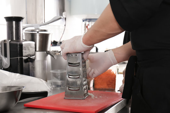 Male chef grating cheese in restaurant kitchen, closeup