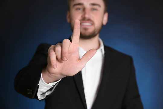 Handsome man in formal suit touching invisible screen on dark background