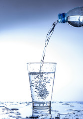 Pouring water and splashing in the glass with reflection on mirror.