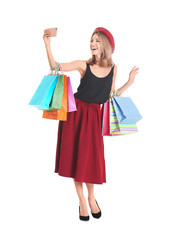 Happy young woman with shopping bags taking selfie on white background