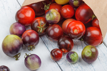Different tomatoes in the paper bag on the white wooden background