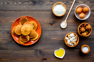 Make fluffy pancakes. Ingredients, cakes and toppings like nuts and honey on dark wooden background top view