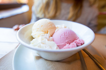 white bowl with two scoops of strawberry and vanilla ice cream and cream, in restaurant table
