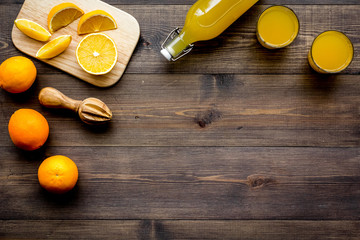 Healthy vitamin drink. Fresh orange juice near fruits and juicer on dark wooden background top view...