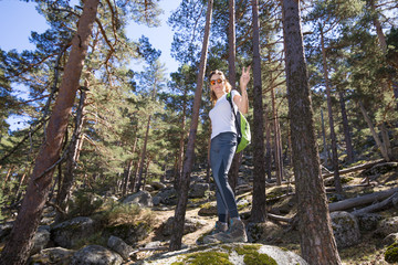 hiker sport woman standing on a great rock in the forest, waving with victory sign in hand, in Navacerrada mountain, Guadarrama Natural Park, Madrid, Spain 
