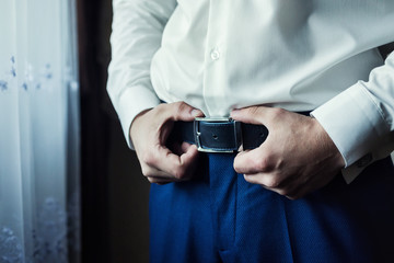 Businessman putting on a belt, fashion and clothing concept,groom getting ready in the morning before ceremony