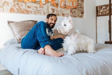 Man relaxed at home sitting in bed with his dog.