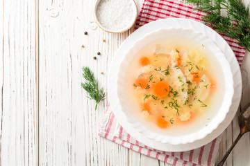Chicken soup with stelline pasta and carrot on white wooden table.