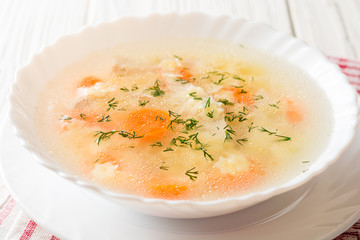 Chicken soup with stelline pasta and carrot on white wooden table.