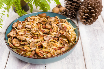 Linguine pasta dish with mushrooms, bacon, walnut and roquefort cheese, served in a blue bowl on white wooden background. Winter food.