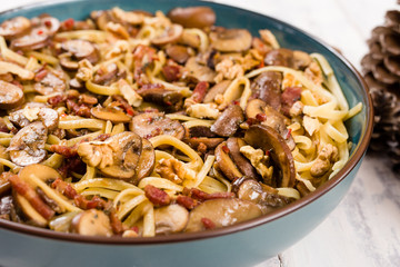 Close up of a linguine pasta dish with mushrooms, bacon, walnut and roquefort cheese, served in a blue bowl on white wooden background.